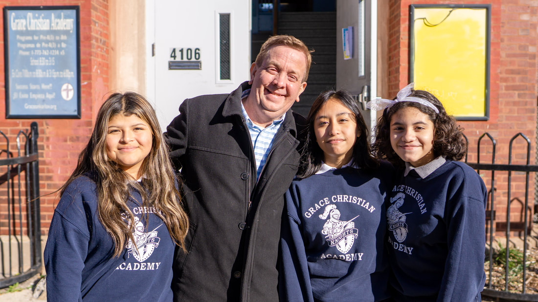 Principal Carlo Giannotta of Grace Christian Academy smiling with three female middle school students on a sunny day in front of the school