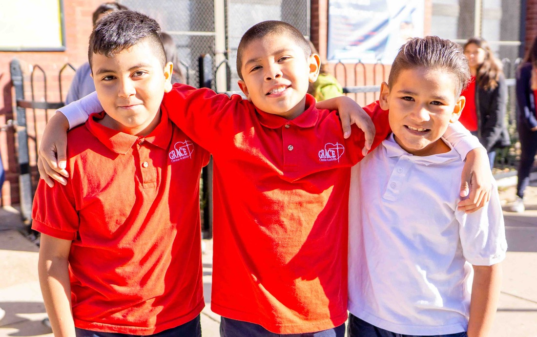 Three male elementary schools students smiling with their arms around each other on a sunny day in front of the school